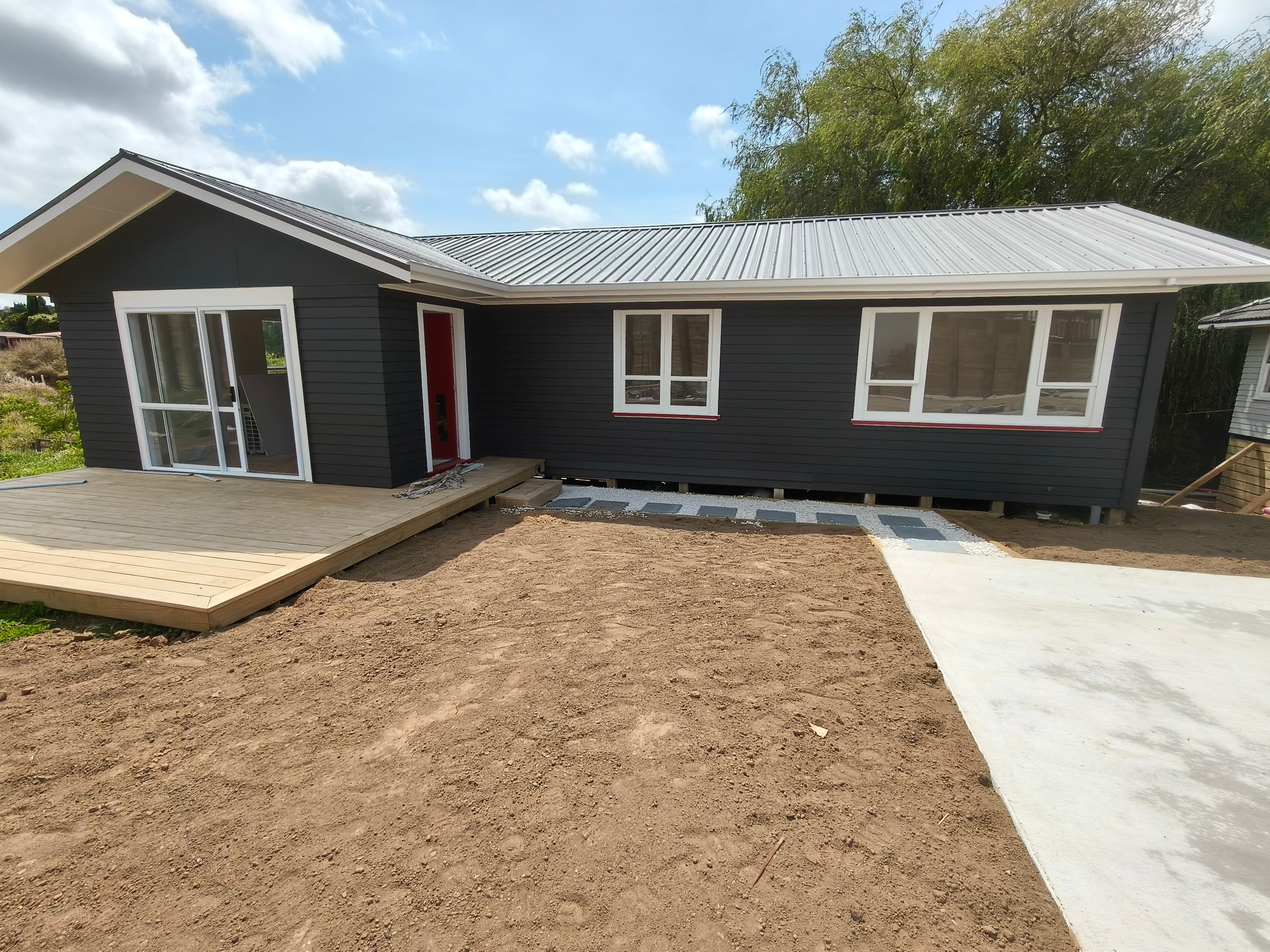 Contemporary relocatable home with dark weatherboards, white trim, and stepping stone path to a red front door.