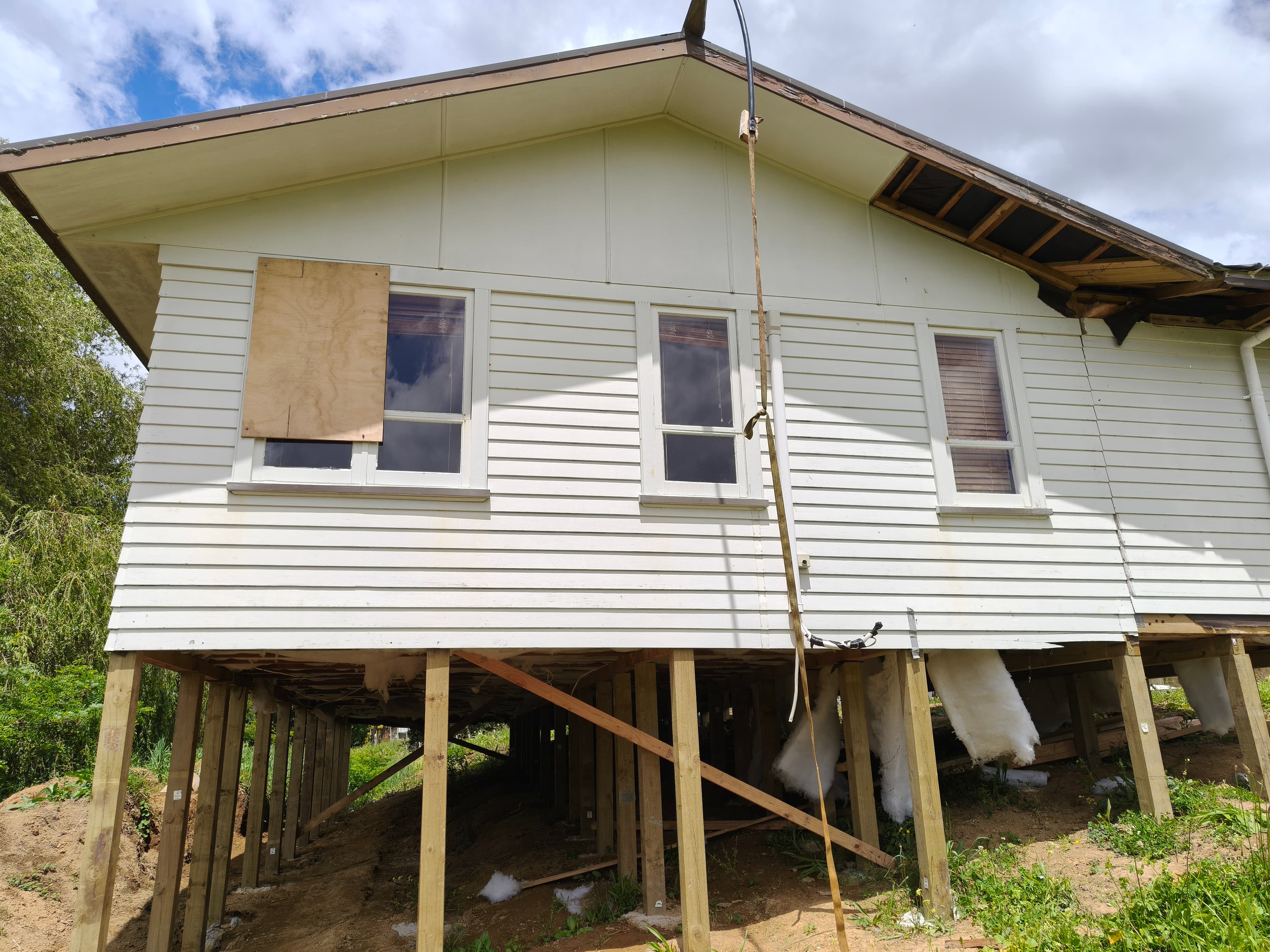 White weatherboard relocatable home elevated on a grid of new timber piles with diagonal bracing.