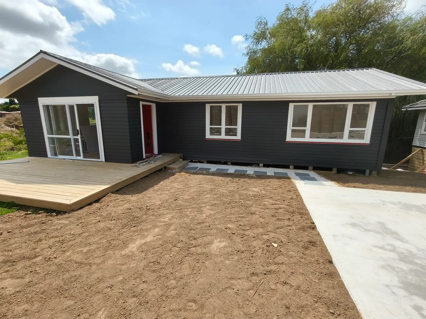 Contemporary relocatable home with dark weatherboards, white trim, and stepping stone path to a red front door.